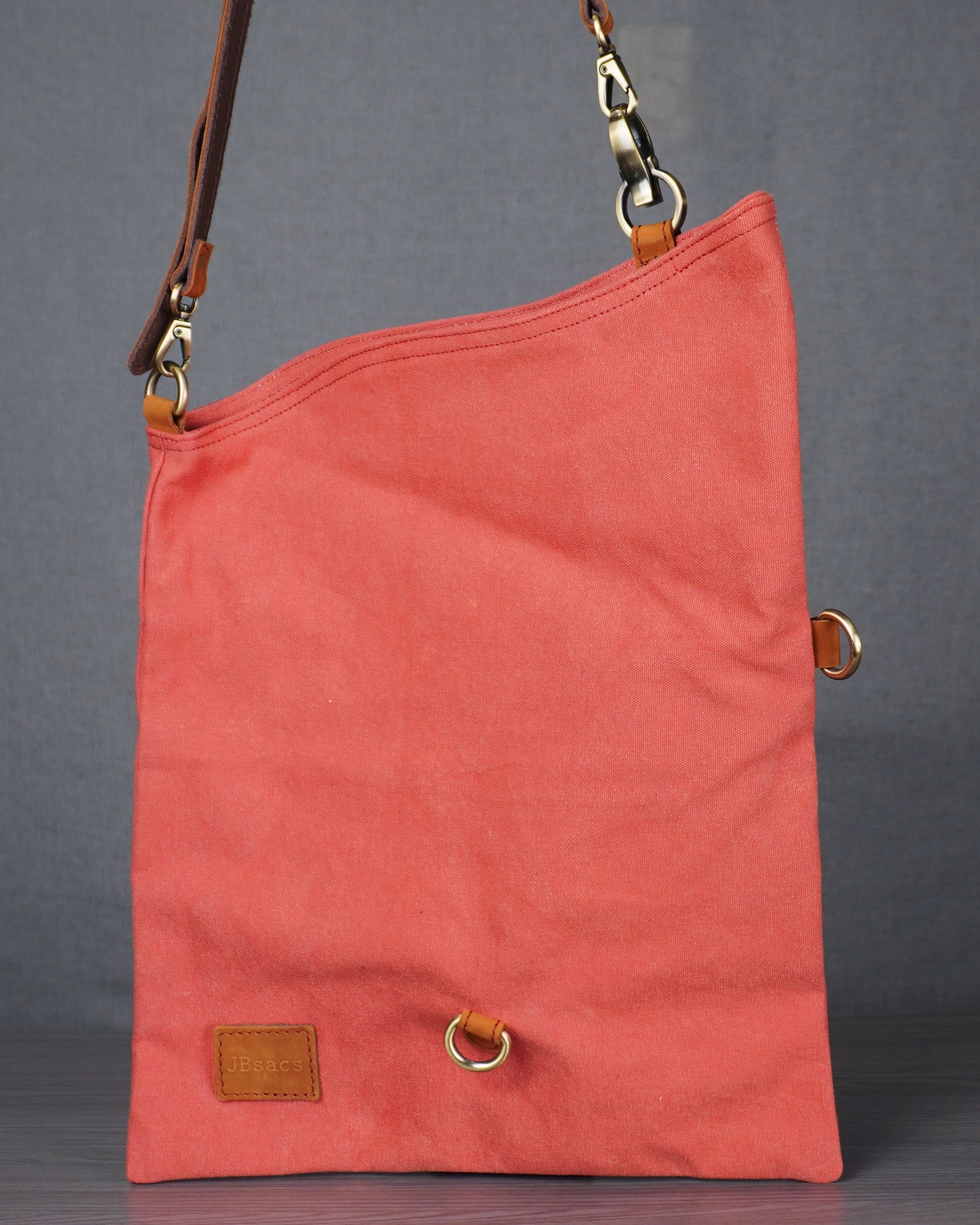Coral-colored bag with a strap on a gray surface against a gray wall.