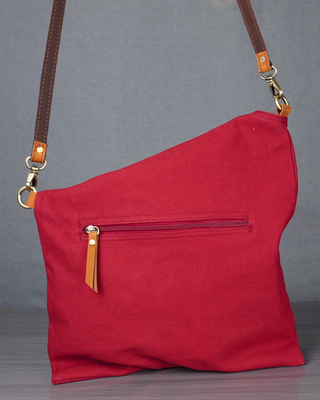 Red shoulder bag with brown strap on a gray surface
