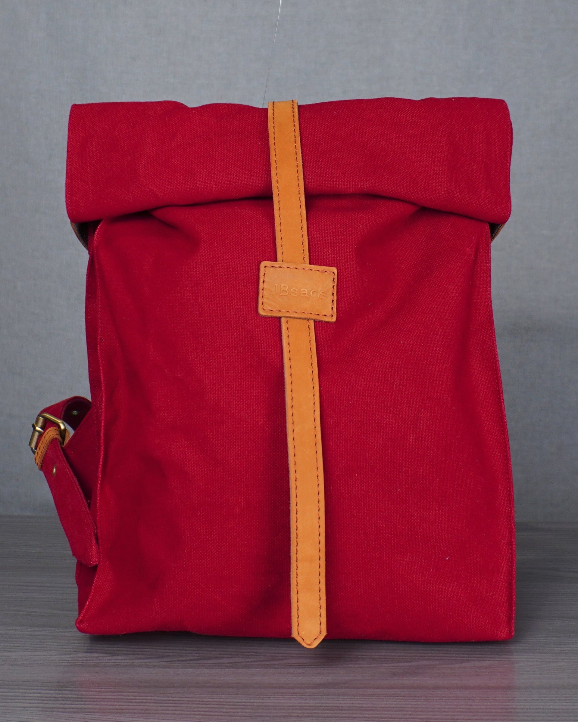Red bag with a yellow strap on a gray surface against a blue wall.