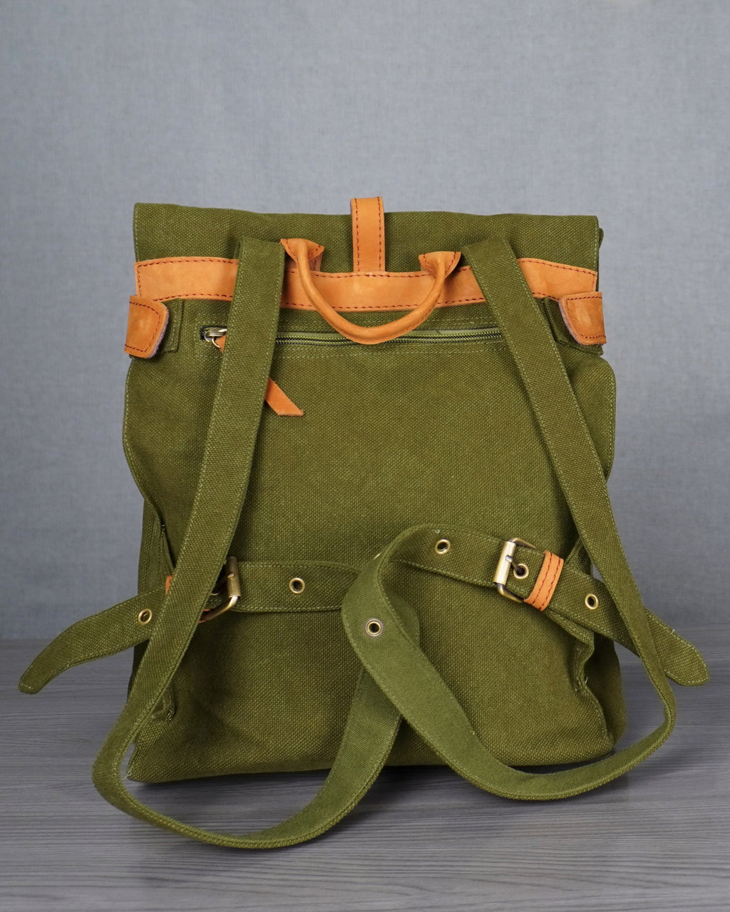 Green backpack with orange accents on a gray floor against a white wall.