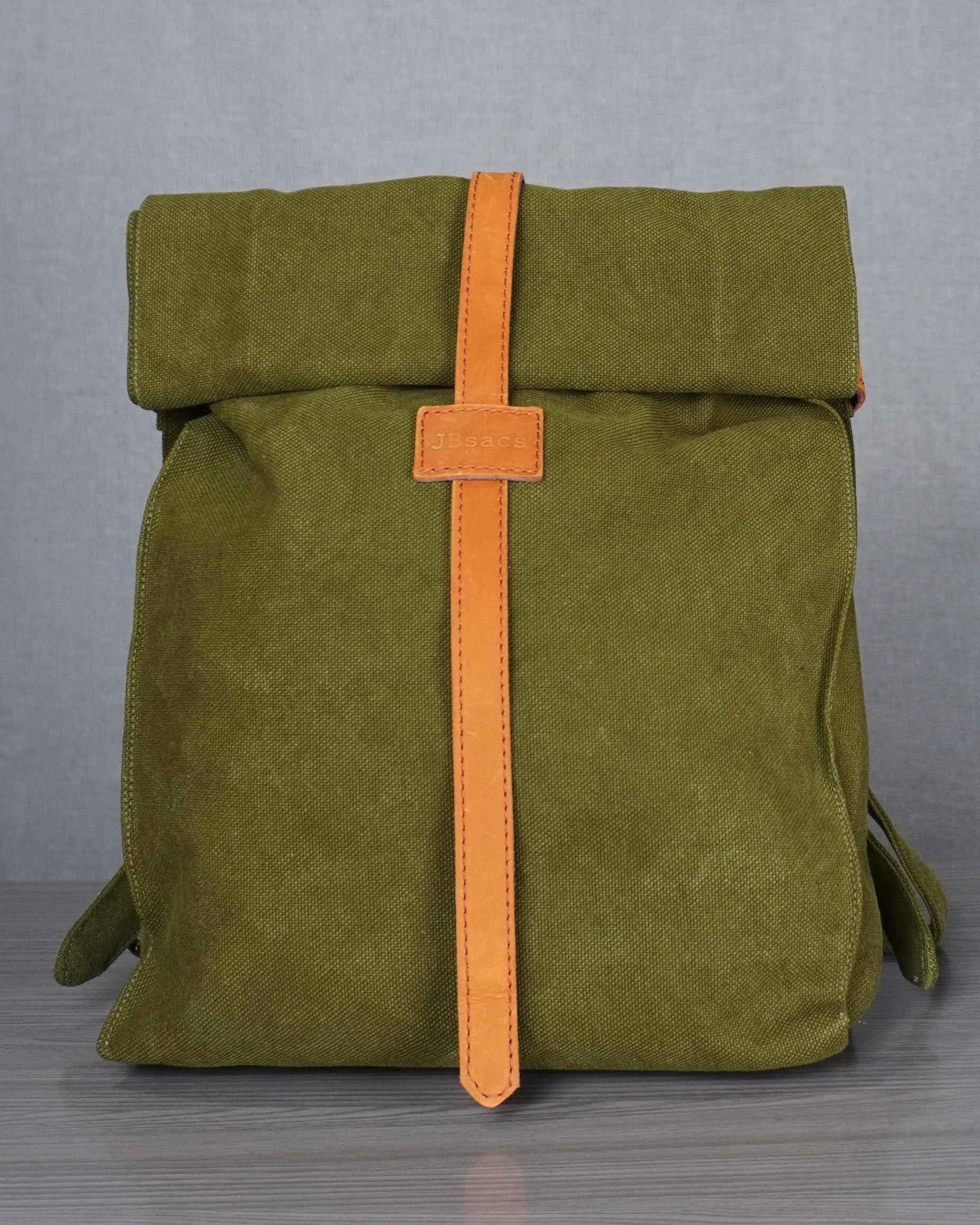 Green backpack with an orange strap on a gray floor against a plain backdrop