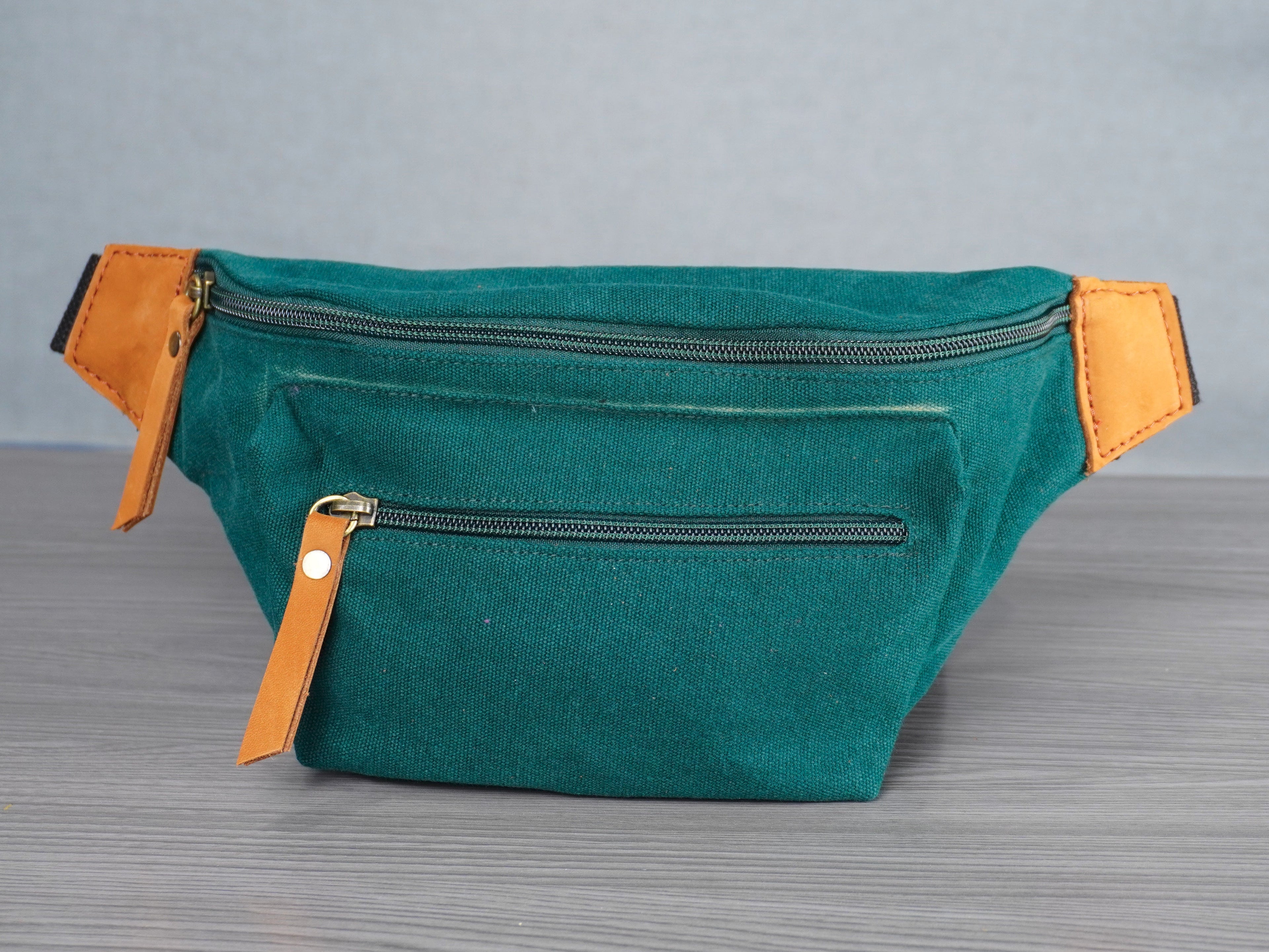 Hunter green waist bag with leather accents on a gray surface