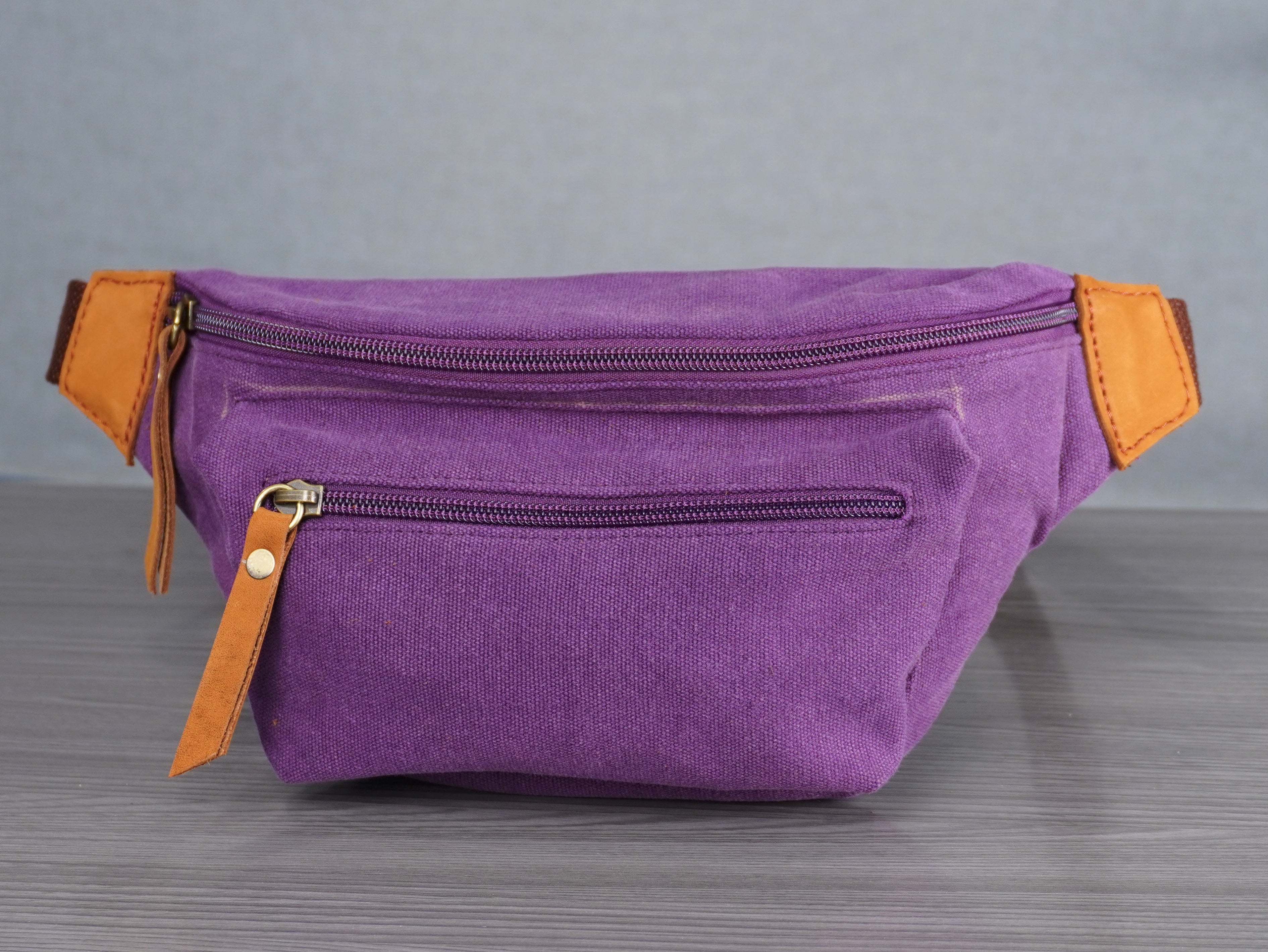 Purple waist bag with orange leather accents on a gray surface