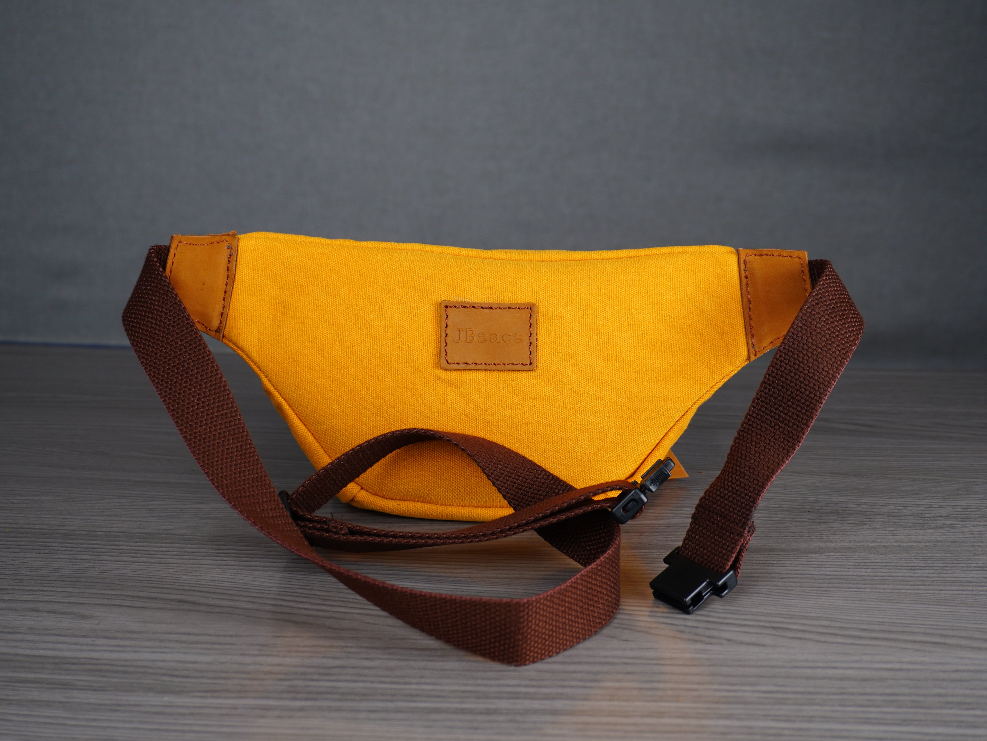 Yellow waist bag with brown strap on a gray surface